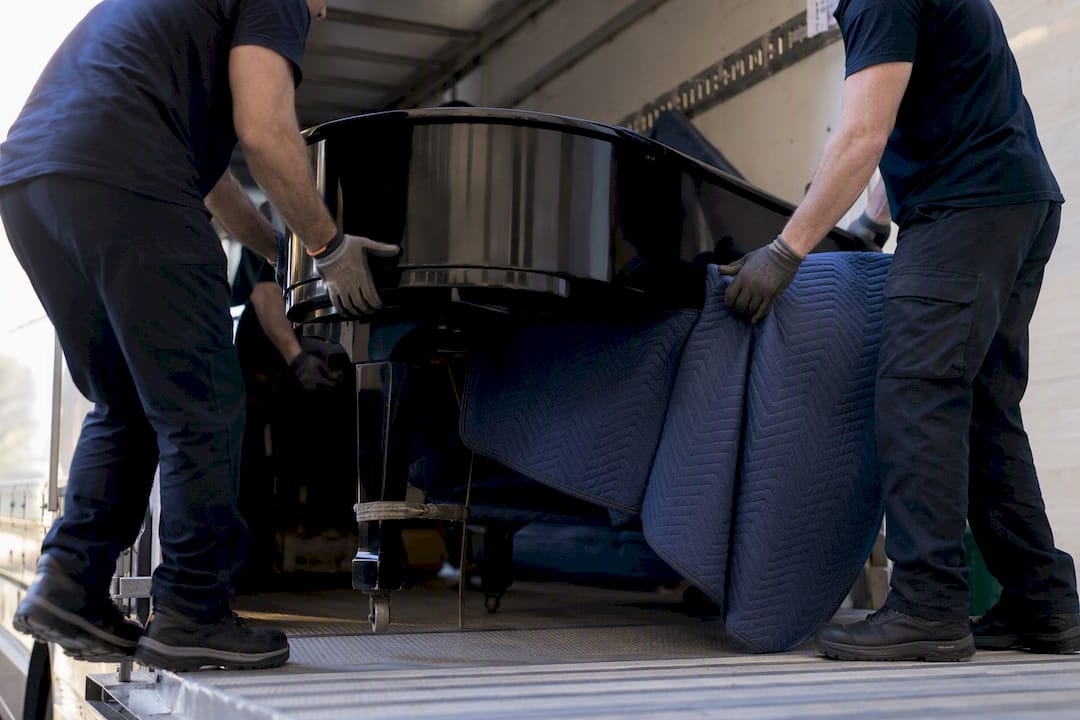 Movers wrapping grand piano inside truck